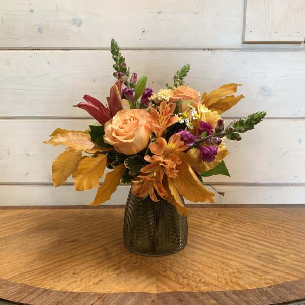 Autumn bouquet of peach and purple flowers in a dark glass vase