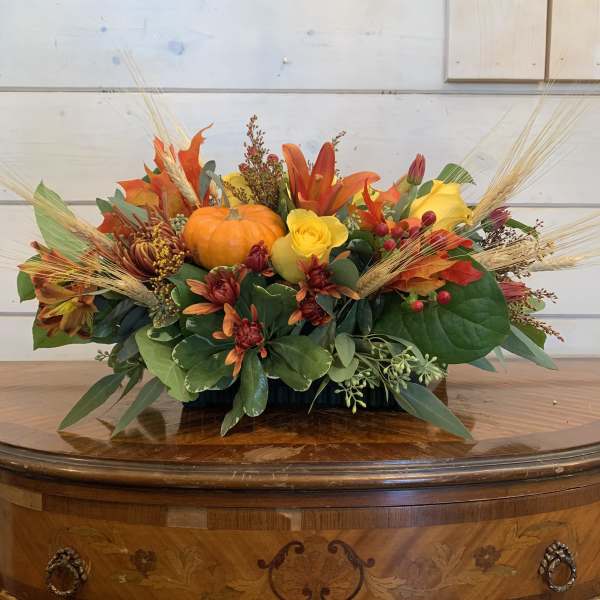 Autumn floral arrangement with pumpkins and orange-yellow flowers in a low container