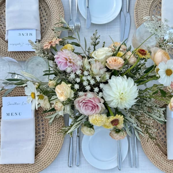 Pastel floral centerpiece on a set dining table with white plates and woven chargers