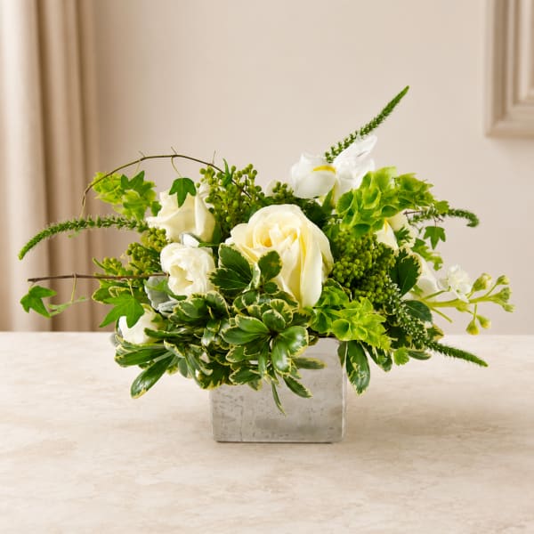 White roses and green flowers arranged in a square glass vase