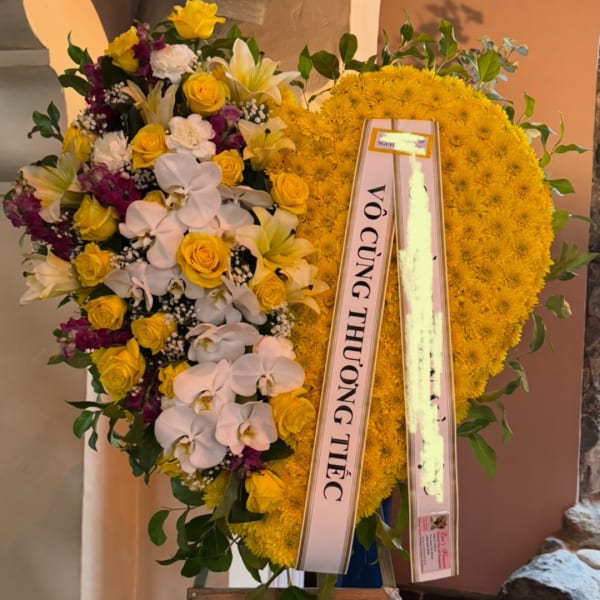 Large yellow and white floral standing wreath with condolence ribbon