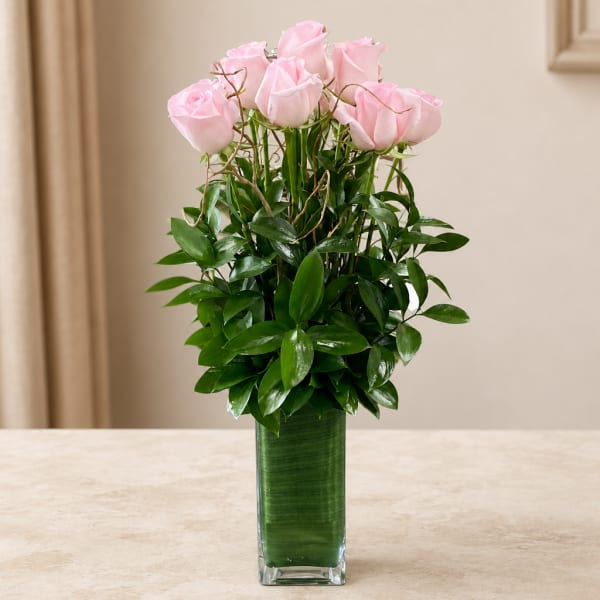 Pink roses arranged in a tall glass vase with dense greenery
