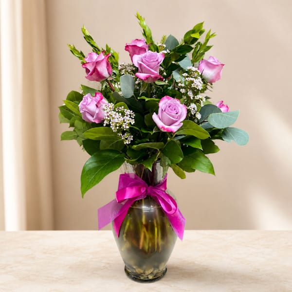 Pink roses arranged in a glass vase with a magenta ribbon