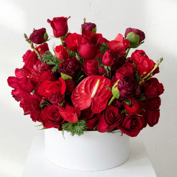 Red rose arrangement in a white round box with an anthurium bloom