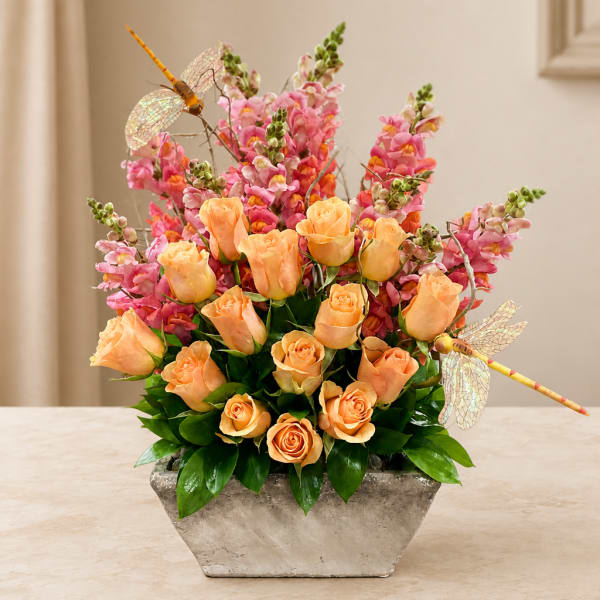 Peach roses and pink snapdragons in a silver vase with dragonfly picks
