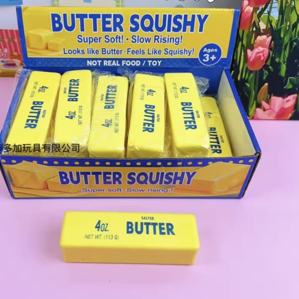 Box of yellow butter-shaped squishy toys on a pink surface