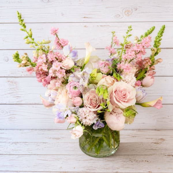 Pastel bouquet of roses, calla lilies, and mixed blooms in a glass vase