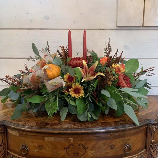 Autumn centerpiece with red candles, orange flowers, and a small pumpkin