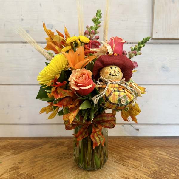 Fall bouquet in a glass vase with a small scarecrow decoration
