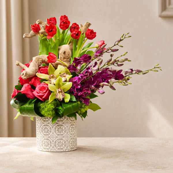 Mixed bouquet of red, pink, and purple flowers in a patterned white vase