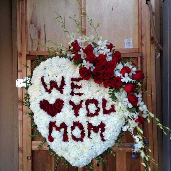 Heart-shaped floral tribute with red roses and white flowers spelling "WE WILL MISS YOU"
