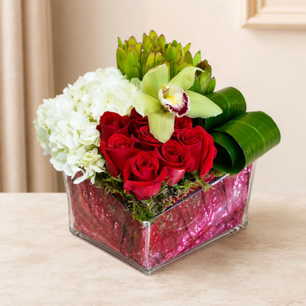Red roses, white hydrangea, and a pale orchid in a square glass vase