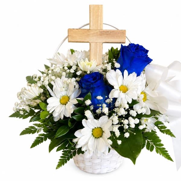 White daisies and blue roses arranged in a basket with a wooden cross