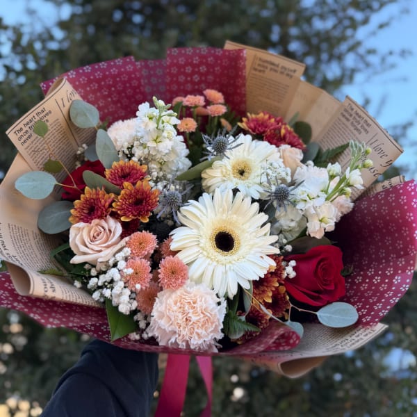 Mixed bouquet with white gerbera daisies, roses, and chrysanthemums wrapped in patterned paper