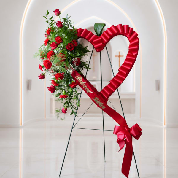 Heart-shaped floral standing spray with red roses and ribbon on an easel
