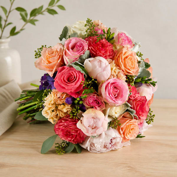 Hand-tied bouquet of pink, peach, and white roses on a table