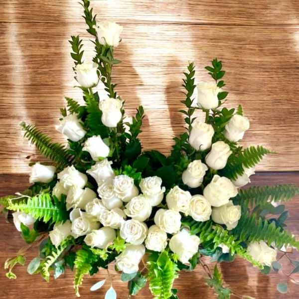 White rose arrangement with fern and greenery on a wooden surface