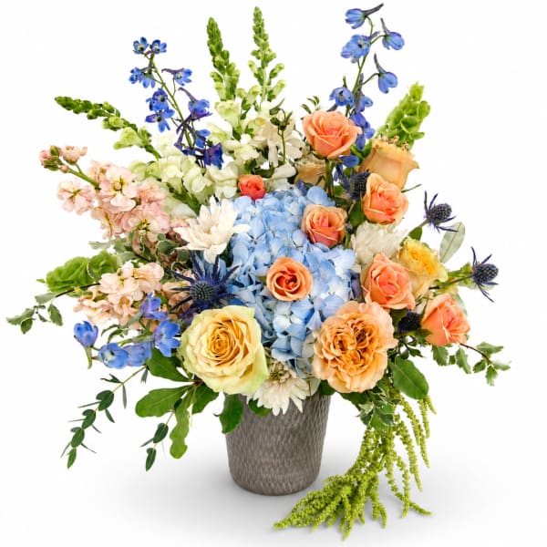 Mixed bouquet of blue, peach, and white flowers in a textured vase