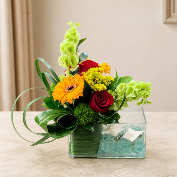 Mixed flower arrangement in a clear rectangular vase with blue stones