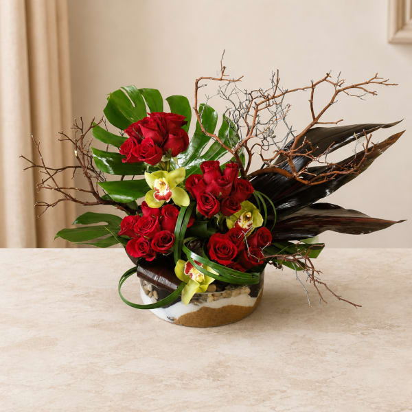 Red roses and yellow orchids in a low glass bowl with branches