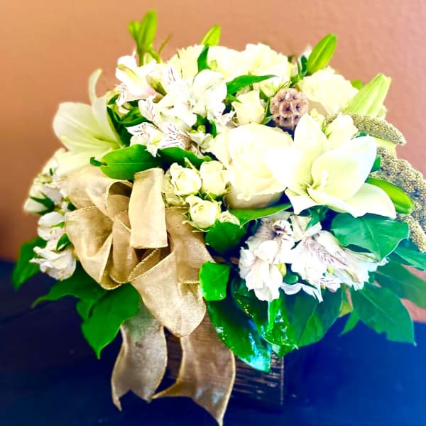 White floral arrangement with a gold ribbon in a dark vase