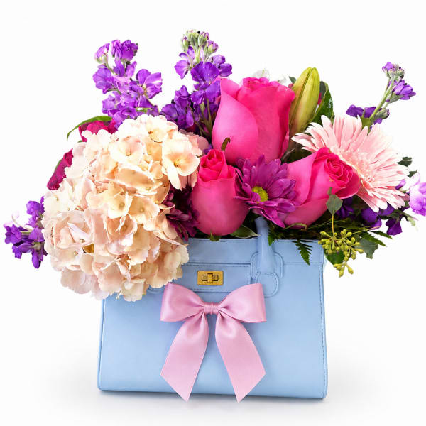 Bouquet of pink and purple flowers in a blue handbag with a pink bow