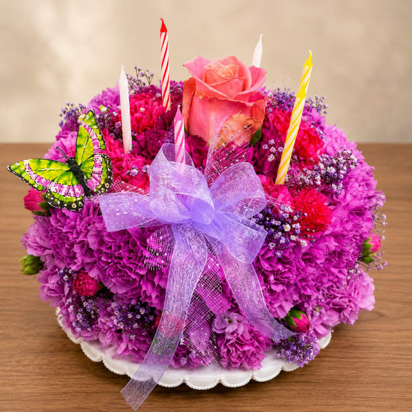 Round pink and purple floral arrangement with candles, a rose, and a ribbon on a white plate