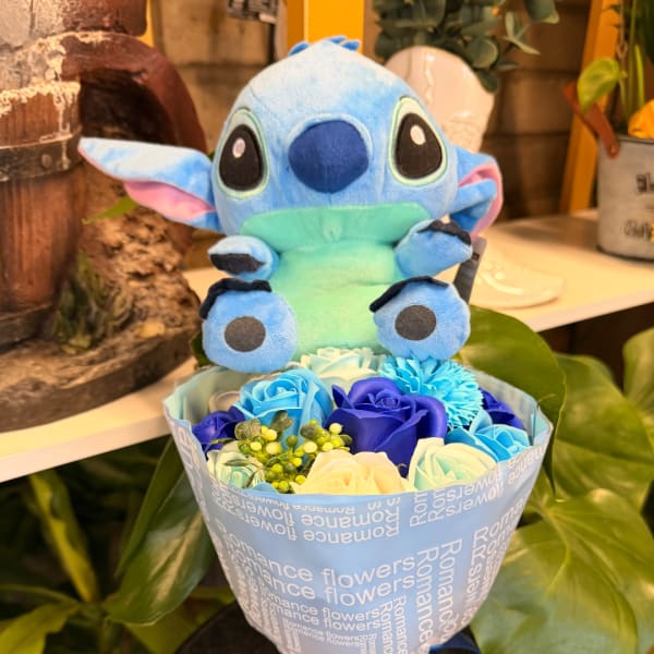Blue plush toy sitting above a bouquet of blue and white roses
