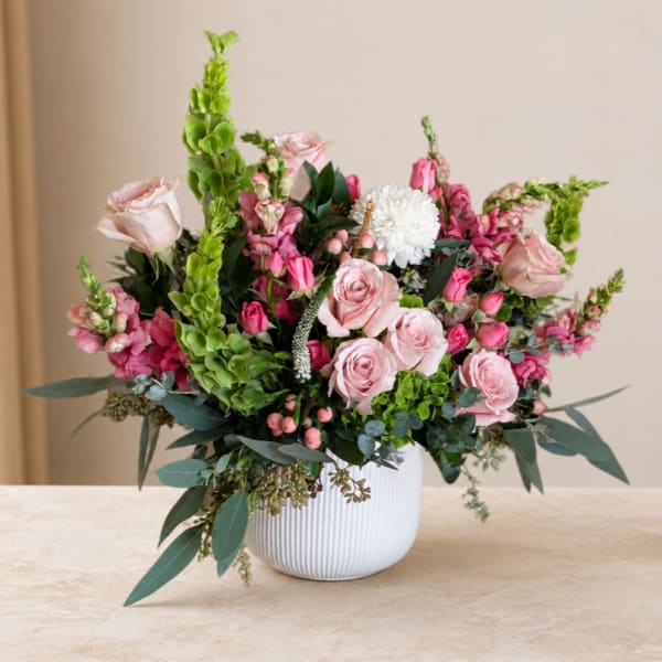Pink roses and mixed blooms arranged in a white vase