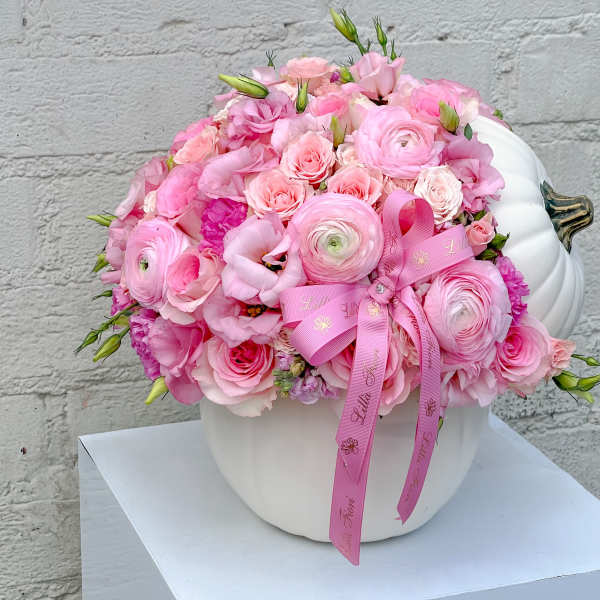 Pink floral arrangement in a white pumpkin-shaped vase with a ribbon bow