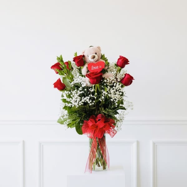 Red roses in a glass vase with a teddy bear and heart topper