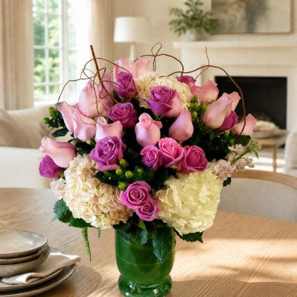 Pink and purple roses with hydrangeas in a green glass vase