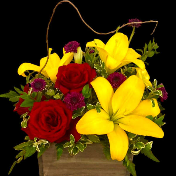 Red roses and yellow lilies in a wooden basket with purple accents