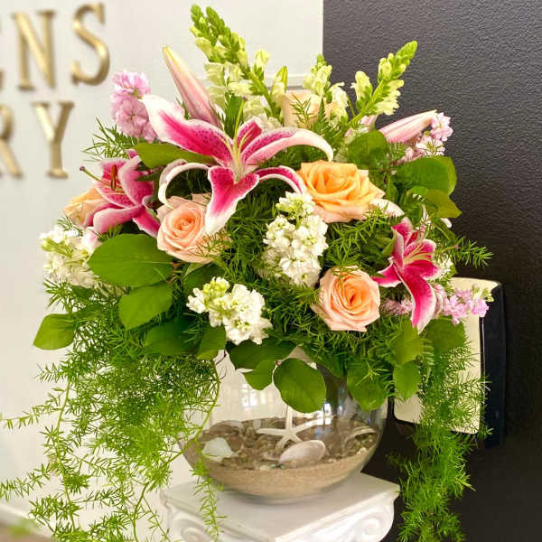 Pink lilies and peach roses arranged in a glass bowl vase