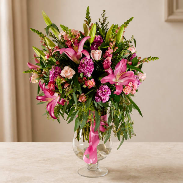 Pink lilies and roses arranged in a clear glass vase with a ribbon