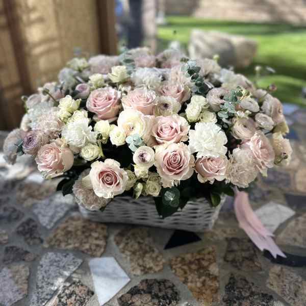Basket arrangement of pale pink and white roses with soft filler flowers