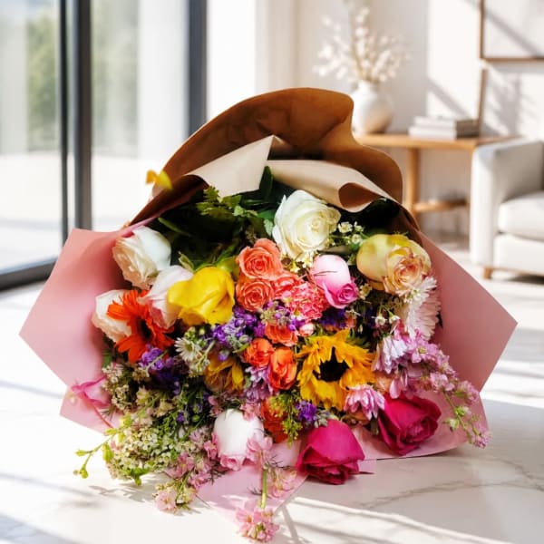 Mixed bouquet of roses, sunflowers, and daisies wrapped in pink paper