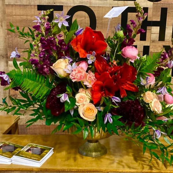Large mixed floral arrangement in a gold vase with red, pink, and purple blooms