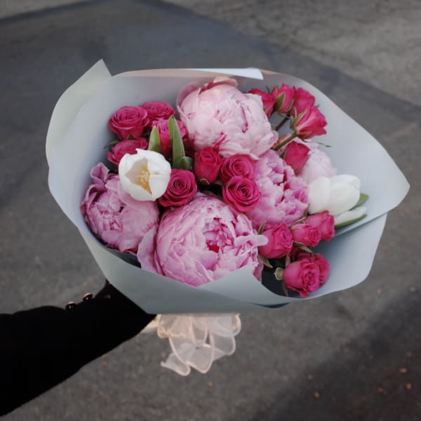Handheld bouquet of pink peonies and roses wrapped in pale paper