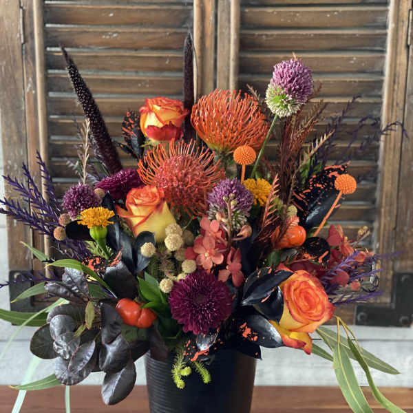 Colorful floral arrangement in a black vase with orange roses and purple blooms