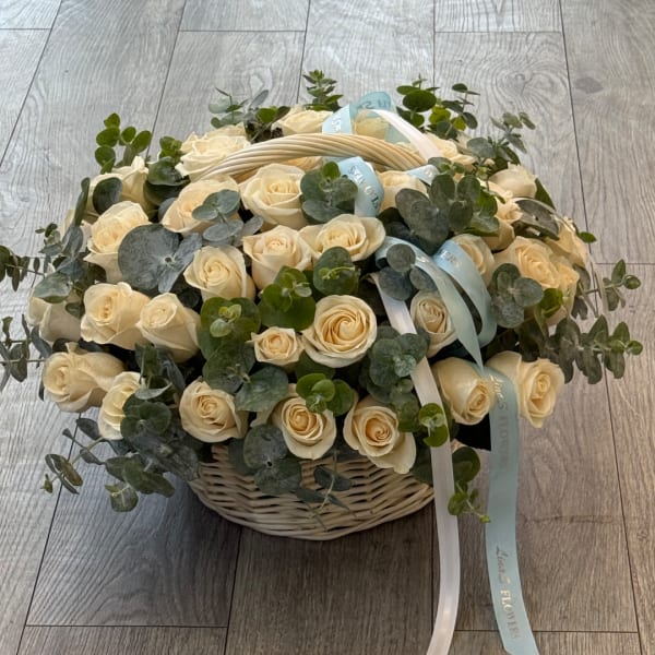 Cream roses in a wicker basket with eucalyptus and pale blue ribbons