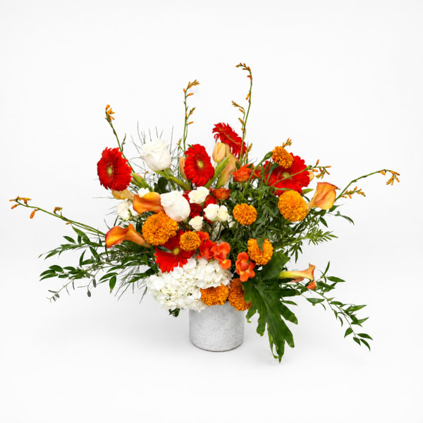 Bright mixed flower arrangement in a white vase with red, orange, and white blooms