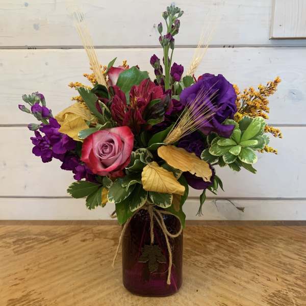 Mixed bouquet in a purple glass vase with a pink rose and purple blooms