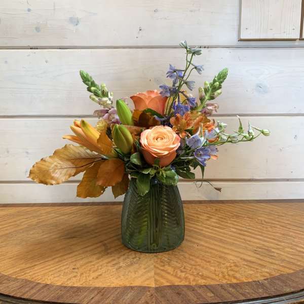 Peach and blue mixed flower arrangement in a green glass vase