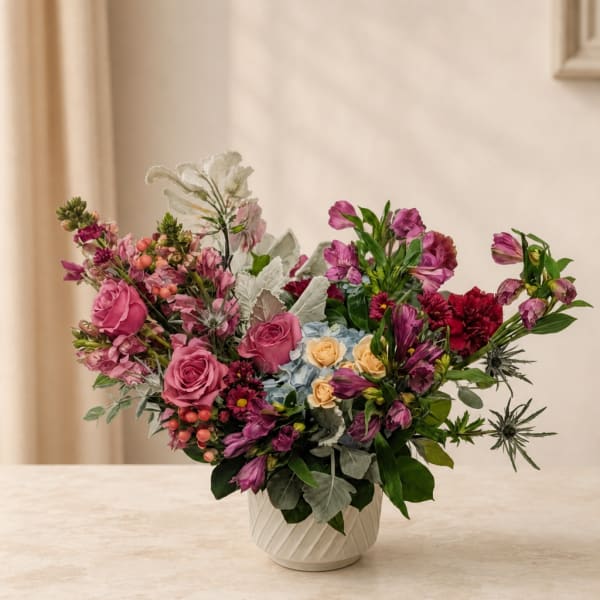 Mixed bouquet of pink and purple flowers in a white vase