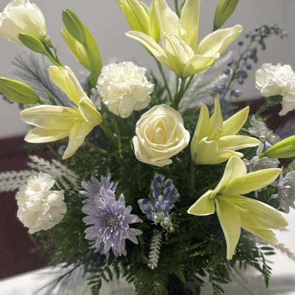 Bouquet of pale yellow lilies, white carnations, and lavender flowers in a vase