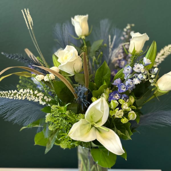 White roses and calla lilies in a glass vase with blue accents