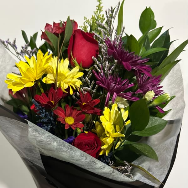Bouquet of red roses, yellow daisies, and purple flowers wrapped in paper