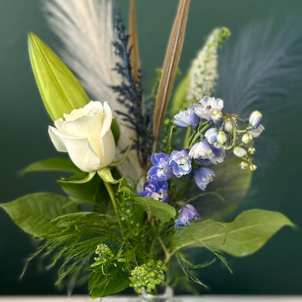 White rose with blue flowers in a clear vase