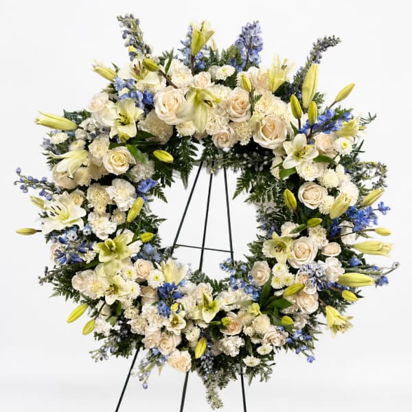 Large white floral wreath on a black stand with cream and blue flowers